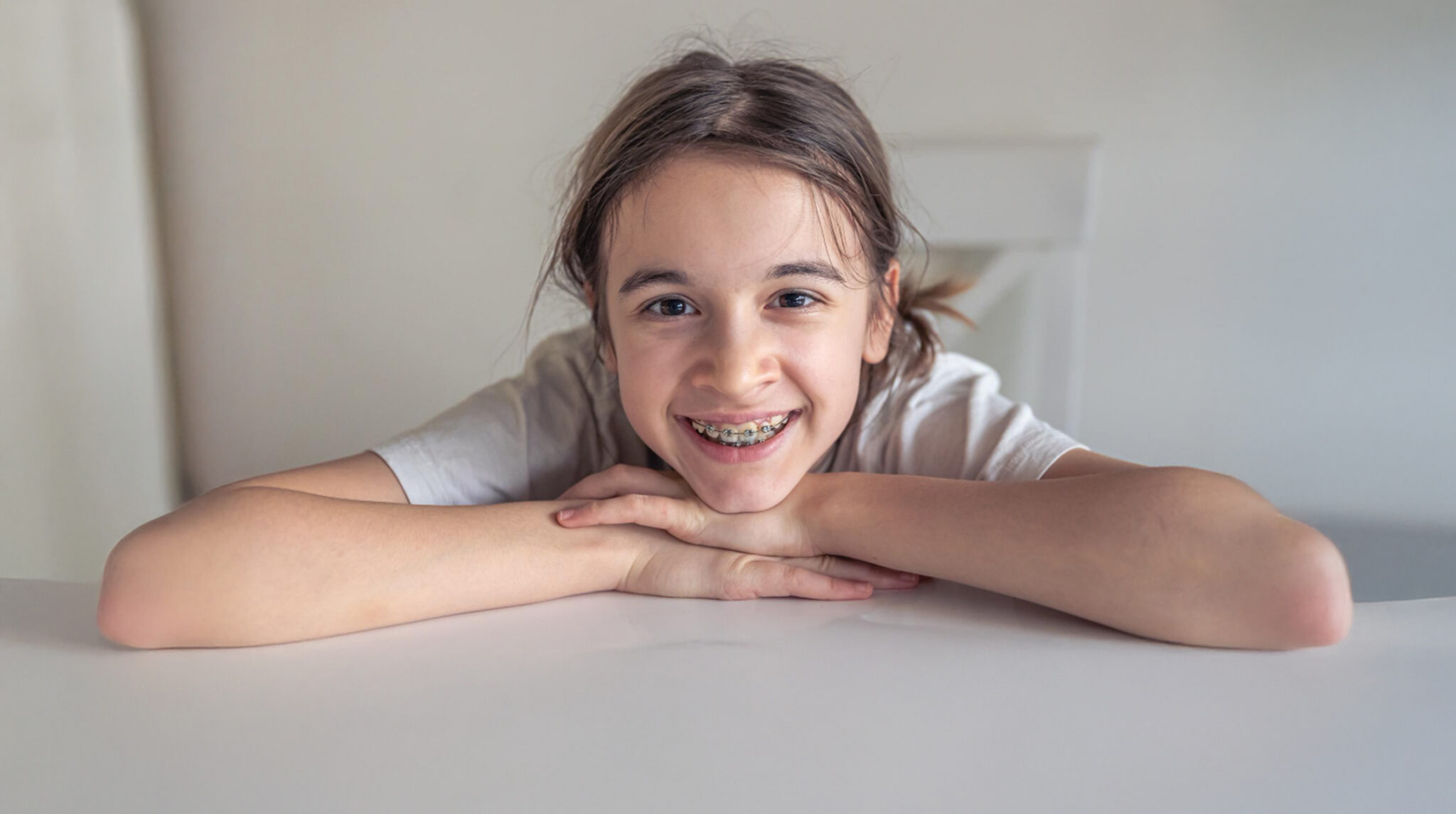 Teen Smiling With Braces Smiling Sitting At A While Table
