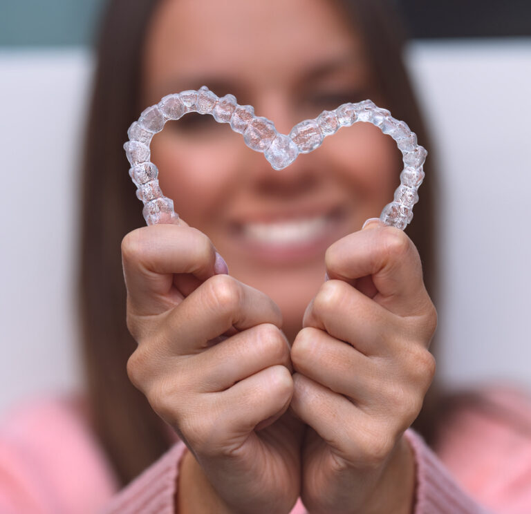 A Woman Holding Clear Aligners Top And Bottom In The Shape Of A Heart
